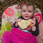 Winnie joined the competition — help win amazing prizes! toddler, child, sandwich, pink_clothing, baby_chair, pigtails, indoor, carpet, bottle, food, cute, smiling, person, seat, playful, face, hair_bow, bright_colors, snack, happy