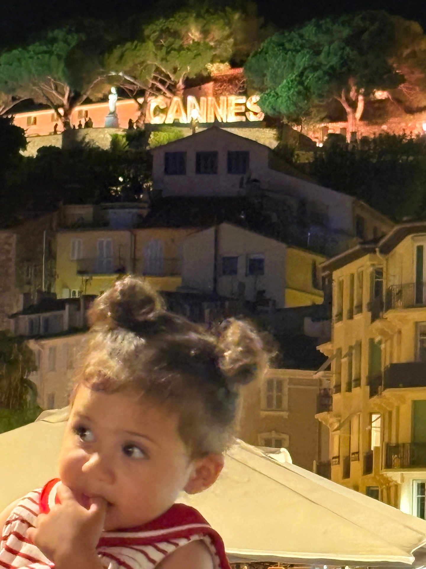 Jana participe au concours pour gagner de l'argent avec cette photo : child, toddler, night, cityscape, buildings, sign, cannes, hair_buns, curious, finger_in_mouth, outdoor, lights, trees, portrait, young_child, person, urban, evening, cute, innocence