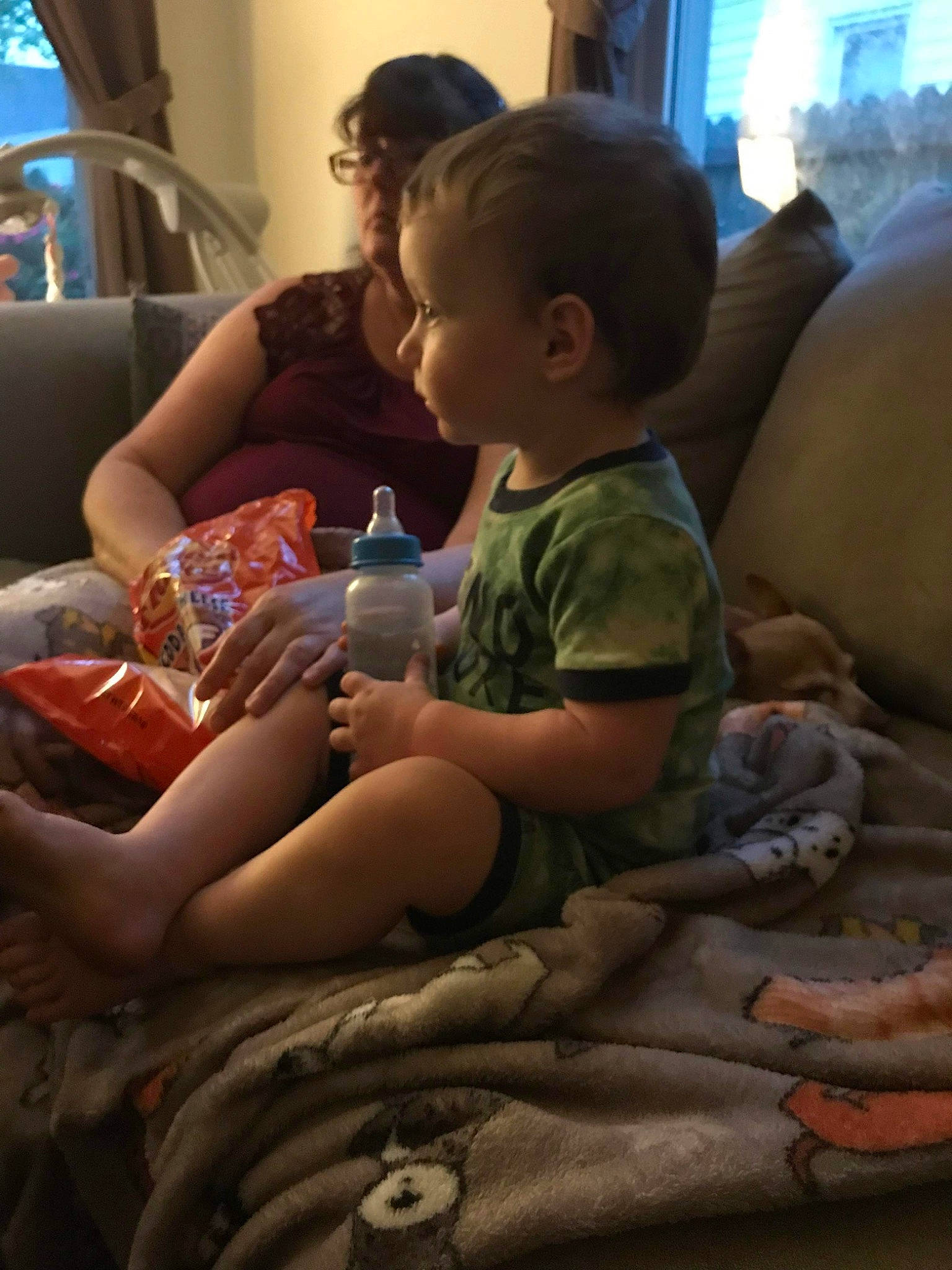 Mary is registered to the contest to win money with this photo: baby, bottle, comfort, drinkware, facial_expression, finger, hair, hairstyle, hand, head, human_body, interaction, lap, leg, living_room, mammal, organ, person, skin, thigh