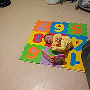 Youna participe au concours pour gagner de l'argent avec cette photo : baby, book, carpet, child, child_playing, christmas_tree, colorful, curious, floor, floor_tiles, foam_mat, holiday, home, indoor, numbers, playtime, relaxing, toddler, toy, yellow_clothing