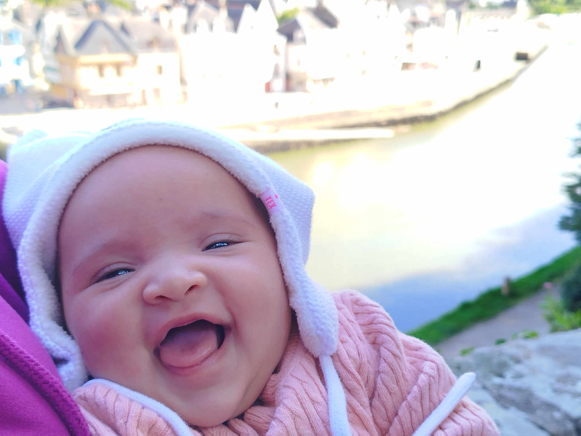 Youna participe au concours pour gagner de l'argent avec cette photo : baby, smiling, happy, infant, face, hat, pink_sweater, tongue_out, outdoor, river, water, blurred_background, person, closeup, cute, child, winter_clothing, nature, daylight, scenic