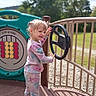 Via is registered to the contest to win money with this photo: child, playground, steering_wheel, tie_dye_clothing, pink_boots, game_panel, outdoor, trees, sunny, happy, person, play, daylight, railing, grass, smile, curly_hair, casual_wear, fun, park