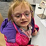 Aviana is registered to the contest to win money with this photo: child, glasses, purple_jacket, pink_jacket, blonde_hair, indoor, desk, paper, mirror, curious_expression, person, clothing, face, young_child, seated, office, furniture, casual_wear, portrait, human