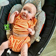 Violet is registered to the contest to win money with this photo: baby, infant, orange_clothing, baby_seat, cushion, face, smile, skin, person, indoor, comfort, cute, newborn, furniture, expression, child, seatbelt, head, legs, arm
