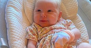 Bobbie joined the competition — help win amazing prizes! baby, infant, smiling, floral_outfit, mittens, padded_seat, window, natural_light, cheeky_smile, cute, indoors, comfort, child, person, skin, hair, head, legs, sitting, cozy