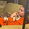 person, cat, couch, orange_clothing, calico_cat, indoor, relaxing, cuddling, furniture, wood_paneling, stone_wall, resting, cozy, home, sleepy, comfort, casual, long_hair, portrait, peaceful