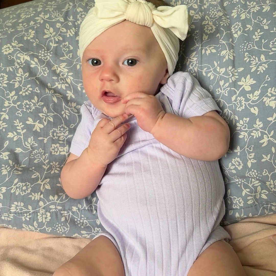 Opal joined the competition — help win amazing prizes! baby, blanket, bow, child, clothing, comfort, cute, expression, eyes, face, hand, headband, indoors, infant, lying_down, onesie, person, pillow, skin, soft