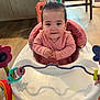 baby, child, pink_clothing, baby_walker, toy, floor, wooden_floor, indoor, smile, face, person, seat, playtime, cute, happy, home, infant, furniture, room, colorful
