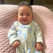 Alanna joined the competition — help win amazing prizes! baby, smiling, infant, onesie, blue_flowers, pink_cushion, cozy, happy, cute, child, portrait, lying_down, soft_texture, indoors, young_child, hand, face, head, comfortable, playful