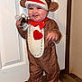 toddler, child, costume, sock_monkey, indoor, floor, wooden_floor, door, keys, smile, happy, red_bow, plush_costume, face, person, cuteness, baby, playful, standing, home