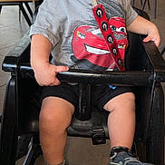 Ricky is registered to the contest to win money with this photo: toddler, child, pacifier, high_chair, shirt, cartoon_car, sneakers, socks, indoor, restaurant, table, chair, floor, baby, clothing, person, footwear, seated, casual, cute