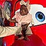 baby, child, person, red_car, cartoon_eye, headband, pink_bib, clothing, barefoot, adult_hands, playful_expression, indoor, toy_car, reflection, bracelet, long_sleeves, pants, cute, portrait, holding