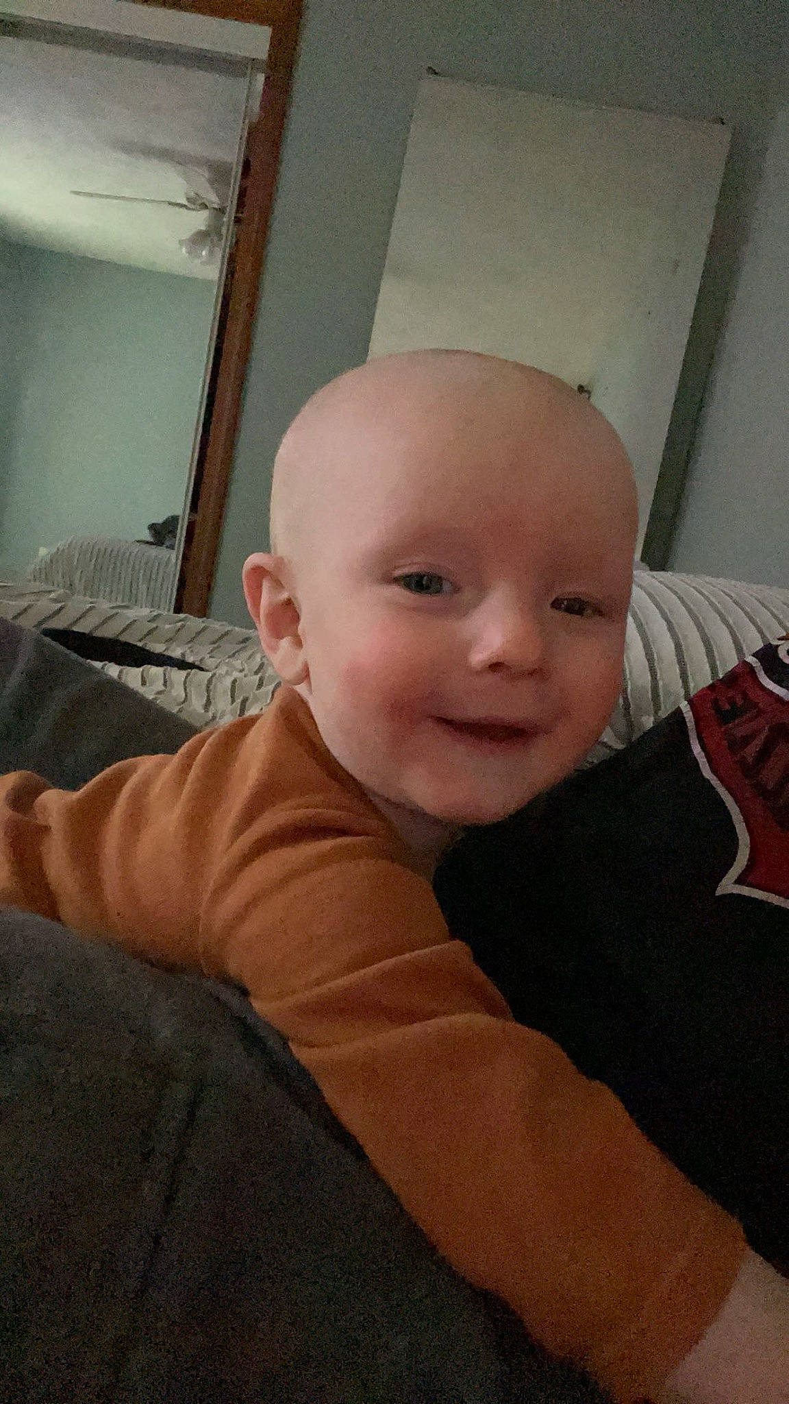 Tate is registered to the contest to win money with this photo: baby, baby_toddler_clothing, cheek, child, comfort, floor, flooring, fun, hardwood, mouth, nose, person, room, sitting, skin, sleeve, smile, t_shirt, thumb, toddler