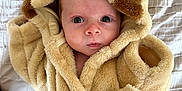 Henry is registered to the contest to win money with this photo: baby, child, face, robe, fur, hood, blanket, bed, soft, cute, curious, indoor, newborn, portrait, clothing, wearing, infant, animal_ears, warm, expression