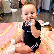 Exavian is registered to the contest to win money with this photo: baby, child, keys, smile, indoor, blanket, floor, sitting, black_clothing, sock, furniture, home, toy, happy, person, flooring, decor, footwear, room, hair