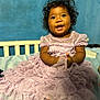 toddler, child, dress, lavender, smile, curly_hair, bed, blue_wall, happy, portrait, indoors, person, clothing, cute, baby, sitting, hands, face, eyes, young