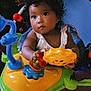 baby, child, indoor, toys, play_station, colorful, curly_hair, drool, face, expression, hands, feet, clothing, seat, wooden_floor, portrait, play, engagement, bright_eyes, cute