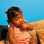 baby, child, infant, pink_clothing, polka_dot, sitting, blanket, blue_wall, curly_hair, indoors, skin, toes, hands, fingers, cute, portrait, young_child, cozy, thoughtful, casual