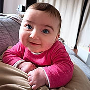 Nina a rejoint le concours — aidez-le/la à gagner de superbes lots ! baby, infant, child, portrait, close_up, blue_eyes, pink_clothing, smile, hands, cheeks, couch, blanket, indoor, curtains, face, hair, soft_texture, cozy, eye_contact, sitting