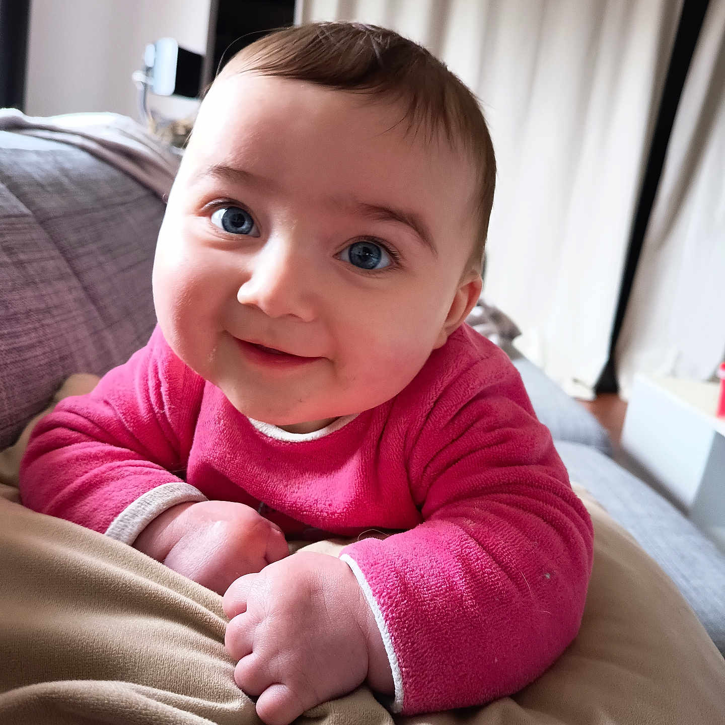 Nina a rejoint le concours — aidez-le/la à gagner de superbes lots ! baby, blanket, blue_eyes, cheeks, child, close_up, couch, cozy, curtains, eye_contact, face, hair, hands, indoor, infant, pink_clothing, portrait, sitting, smile, soft_texture