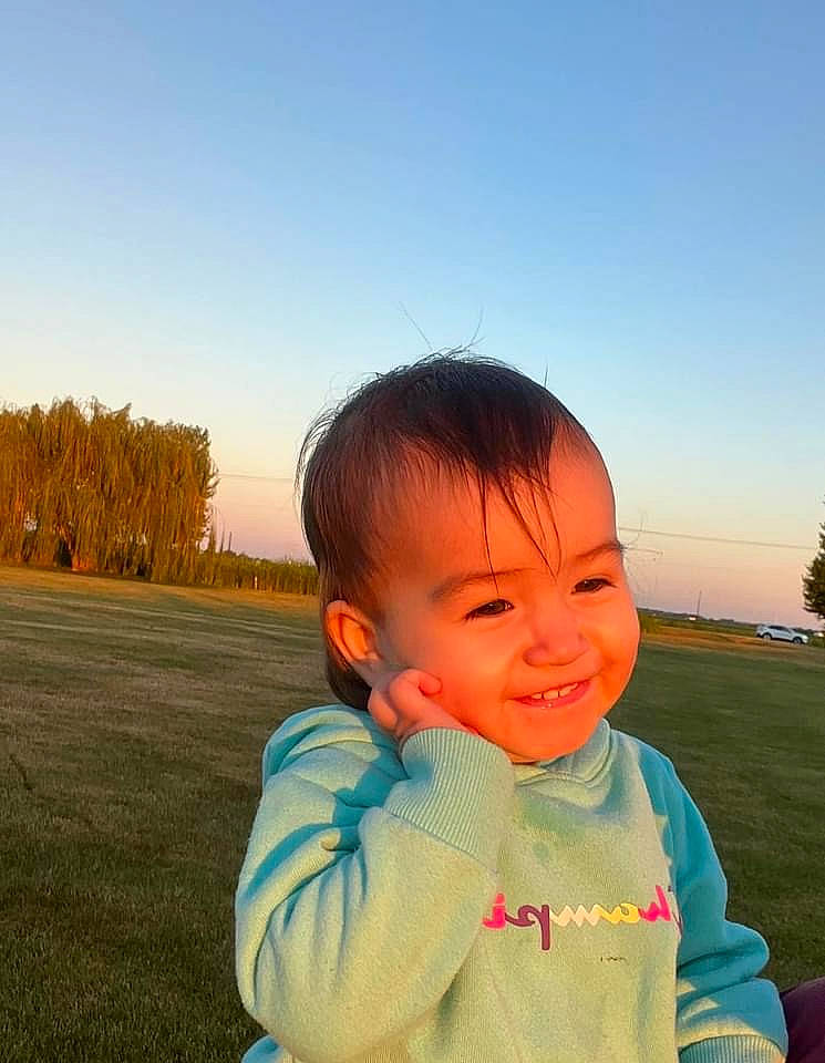 Natalia is registered to the contest to win money with this photo: baby_toddler_clothing, chin, cloud, cool, daytime, face, finger, gesture, grass, hairstyle, happy, joy, leisure, people_in_nature, person, plant, sky, smile, sunlight, toddler