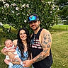Kacee is registered to the contest to win money with this photo: baby, woman, man, family, outdoor, tattoo, flowering_bush, grass, casual_clothing, smile, holding, cap, tank_top, nature, greenery, portrait, people, young_adult, infant, happy