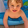 toddler, child, pigtails, smiling, inflatable_pool, water, sunlight, brick_wall, window, outdoor, crawling, happy, skin, face, play, summer, cute, baby, hands, blue