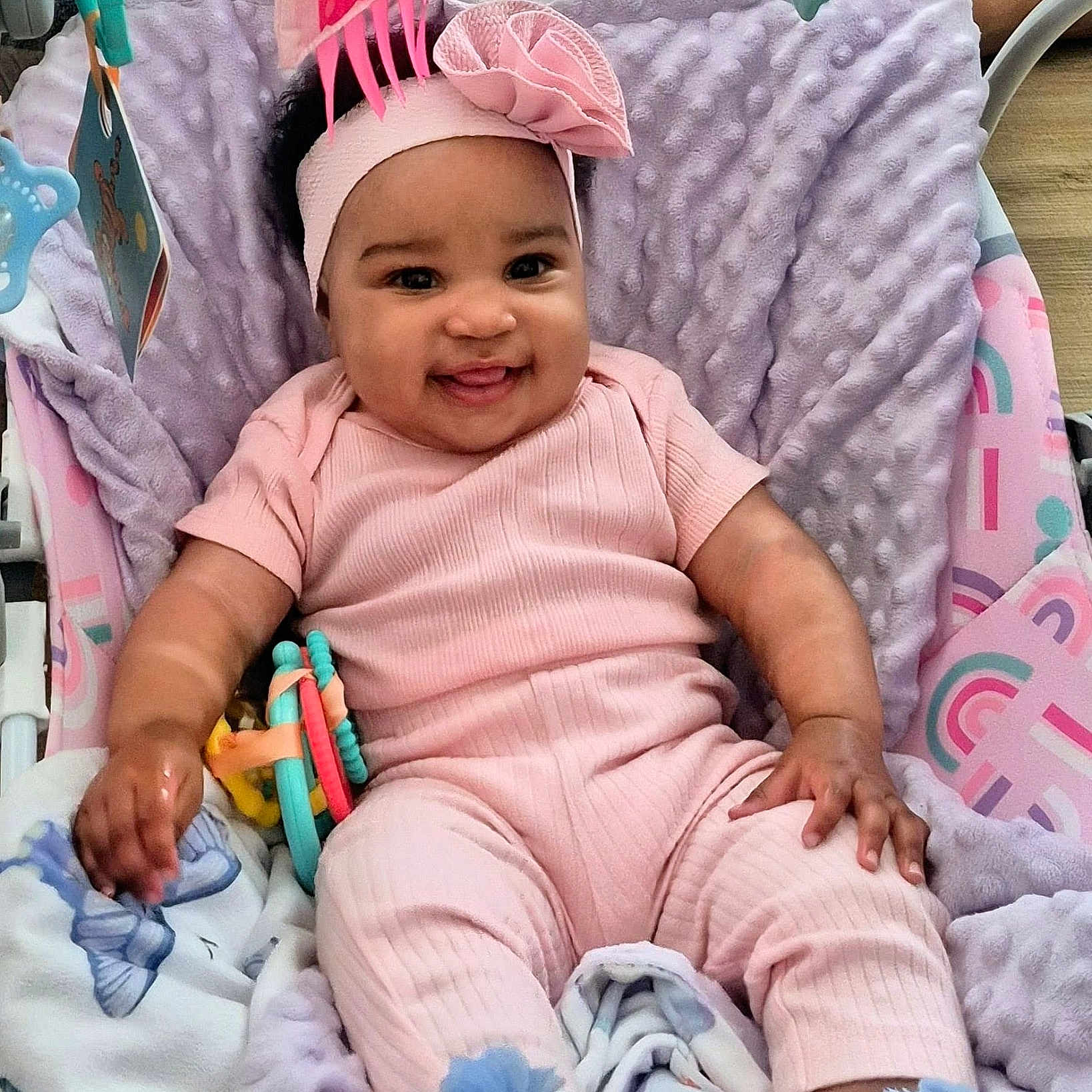 Nevaeh-Celeste is registered to the contest to win money with this photo: baby, infant, smiling, pink_clothing, headband, bow, blanket, toy, baby_seat, cozy, happy, cute, child, cheerful, indoors, soft_texture, person, footwear, hand, face