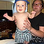baby, bedroom, box, cabinet, cap, casual, checkered_shorts, child, furniture, glasses, happy, holding, indoor, lip_piercing, person, skin, smiling, tattoo, television, woman