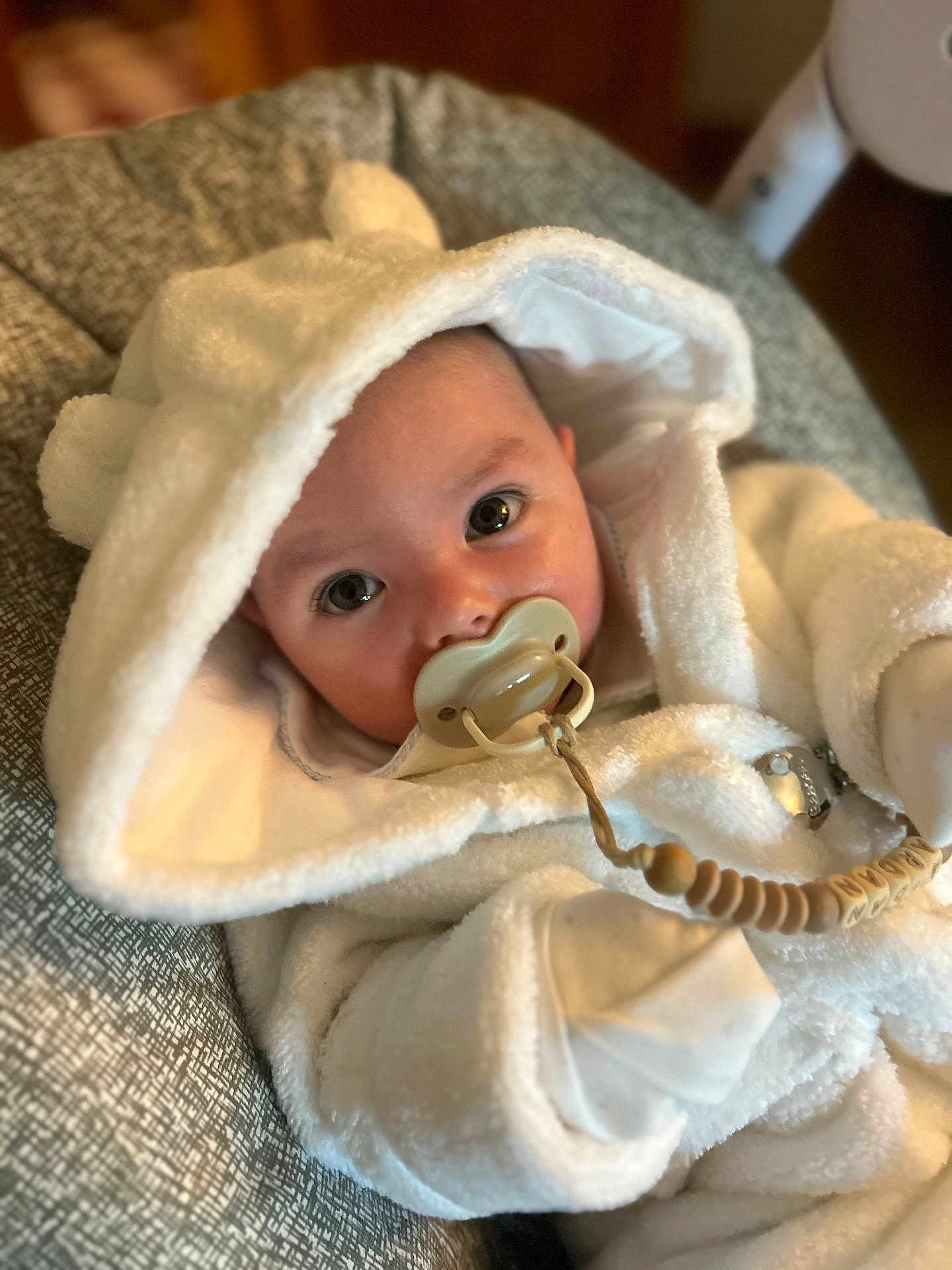 Ardán-John joined the competition — help win amazing prizes! baby, pacifier, hood, white_clothing, cushion, infant, close_up, soft_texture, beaded_clip, indoor, cute, portrait, child, sleepwear, warm_clothing, resting, young_child, face, big_eyes, cozy