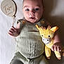 Ardán-John is registered to the contest to win money with this photo: baby, infant, two_months, knitted_clothing, plush_toy, giraffe_toy, wooden_sign, milestone, blanket, portrait, cute, child, smiling, hand, face, lying_down, soft_texture, button, baby_clothes, indoors