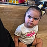 Bella is registered to the contest to win money with this photo: toddler, child, girl, sitting, indoor, wooden_bench, bandage, bow, hair_accessory, white_tshirt, black_shorts, shoe, sock, serious_expression, face, person, casual_clothing, reflection, restaurant, background_people