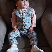 Israel is registered to the contest to win money with this photo: toddler, child, boy, plaid, vest, bow_tie, shirt, pants, white_shoes, sitting, armchair, indoors, curious, portrait, cute, fashion, baby, clothing, footwear, furniture