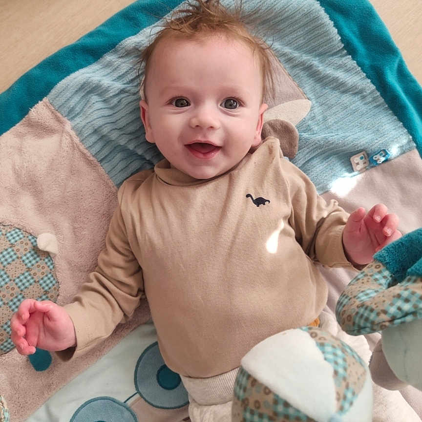 Logan a rejoint le concours — aidez-le/la à gagner de superbes lots ! baby, smiling, infant, blanket, patchwork, toy, soft_toy, happy, lying_down, cute, child, indoors, clothing, long_sleeve, face, head, skin, eyes, hands, hair