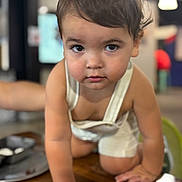 Mateo joined the competition — help win amazing prizes! toddler, child, baby, overalls, crawling, wooden_table, indoor, curious, face, skin, eyes, hair, hand, furniture, background_blur, person, cute, young_child, expression, focus