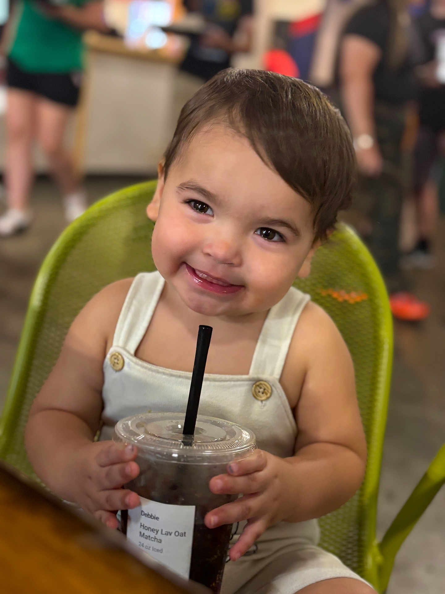 Mateo joined the competition — help win amazing prizes! toddler, child, smile, drink, iced_beverage, chair, white_clothing, cafe, happy, portrait, indoor, cute, person, hair, skin, table, holding, beverage, black_straw, buttoned_overalls