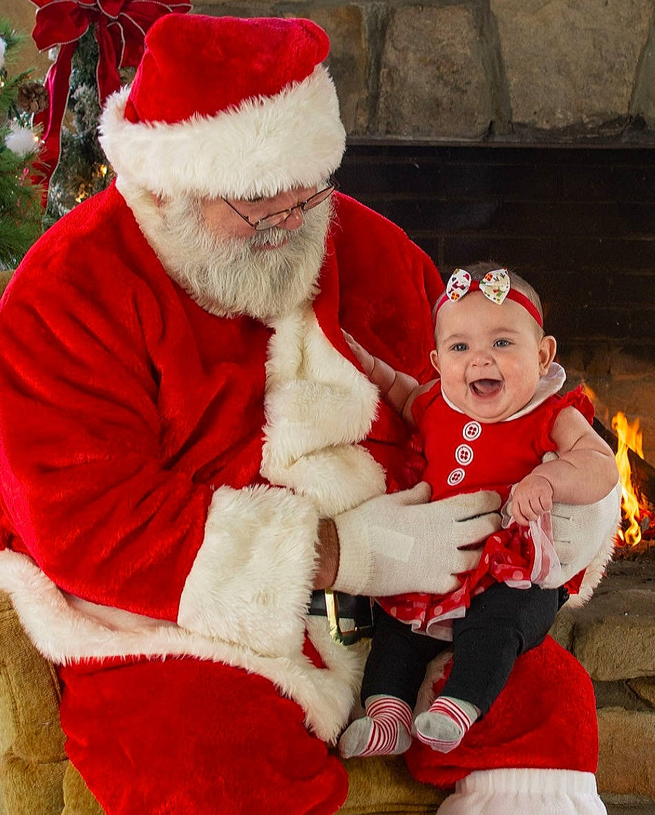 Primrose is registered to the contest to win money with this photo: beard, christmas, christmas_decoration, christmas_eve, costume_hat, event, fur_clothing, happy, hat, head, headwear, holiday, human_body, joy, lap, outerwear, person, red, santa_claus, smile