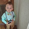 child, boy, toddler, portrait, standing, smiling, bow_tie, suspenders, shirt, trousers, barefoot, game_controller, indoors, door, wall, wooden_floor, vent, fashion, formalwear, photography