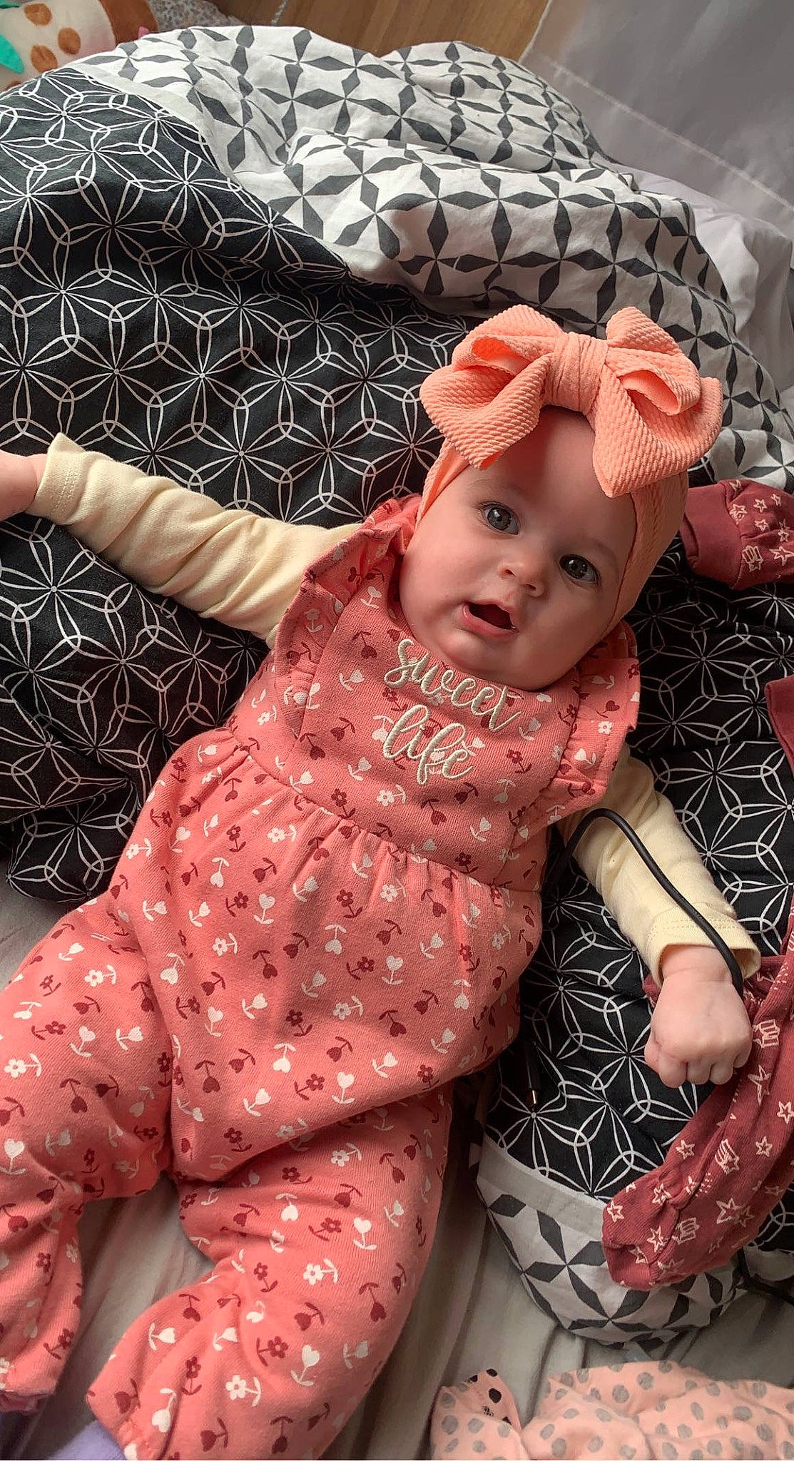 Mia participe au concours pour gagner de l'argent avec cette photo : baby, baby_toddler_clothing, cheek, child, doll, dress, fashion_accessory, fawn, happy, headwear, human_body, magenta, pattern, peach, person, pink, sitting, skin, sleeve, textile