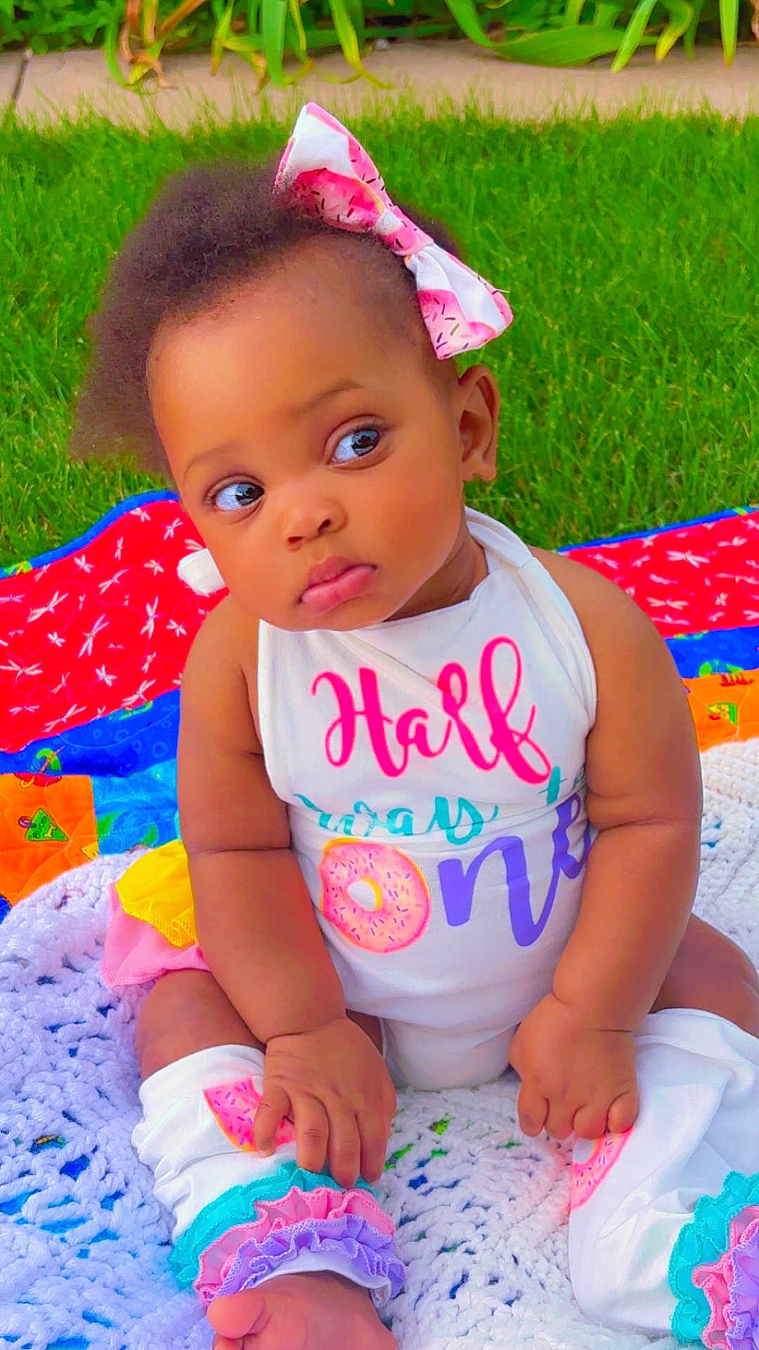 Elorah joined the competition — help win amazing prizes! baby, child, grass, outdoor, quilt, colorful, bow, clothing, cute, infant, sitting, face, portrait, leg_warmers, pink, white, expression, summer, nature, toddler