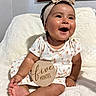 baby, infant, smiling, sitting, headband, dress, wooden_sign, five_months, blanket, indoors, cute, happy, child, portrait, skin, person, foot, hand, face, milestone