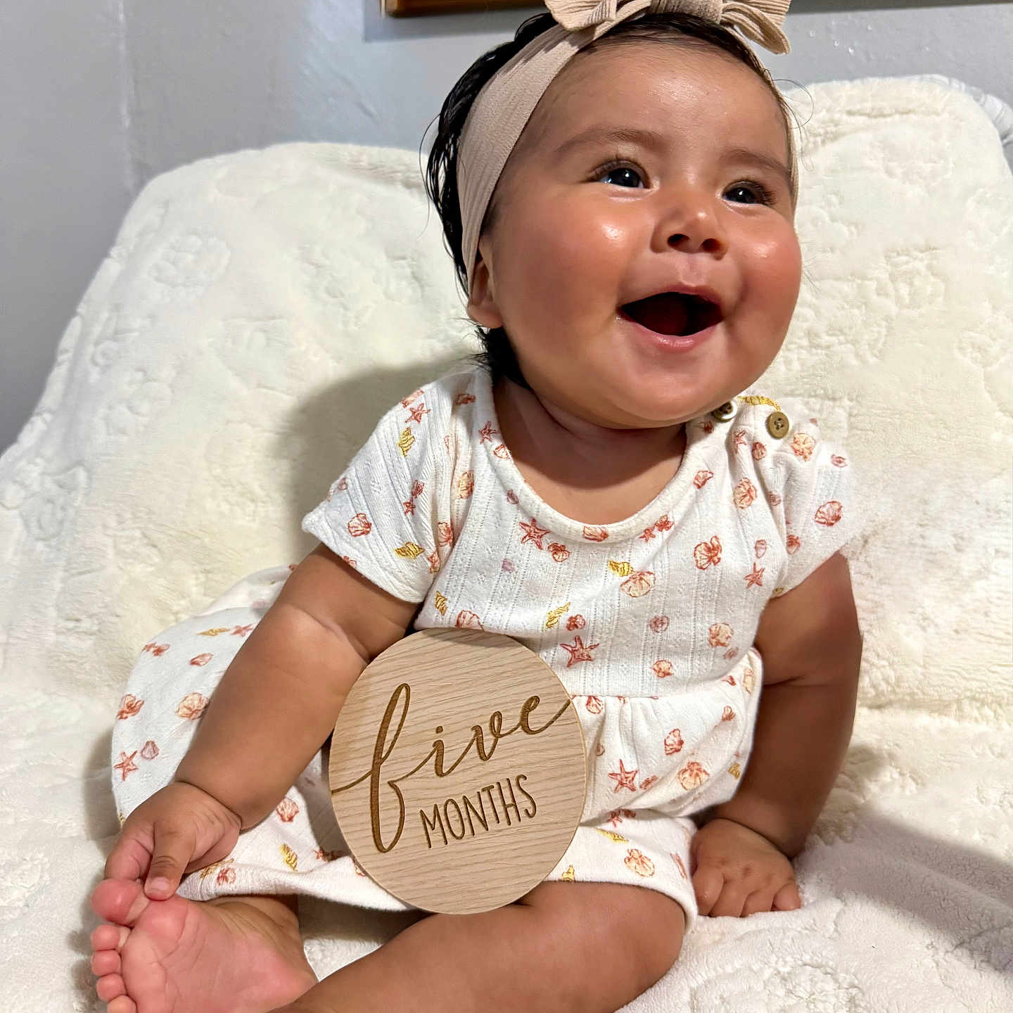Ellie joined the competition — help win amazing prizes! baby, infant, smiling, sitting, headband, dress, wooden_sign, five_months, blanket, indoors, cute, happy, child, portrait, skin, person, foot, hand, face, milestone
