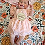 Violet is registered to the contest to win money with this photo: baby, infant, smiling, dress, blanket, floral_pattern, pink, orange, cheerful, cute, lying_down, milestone, child, happy, skin, feet, hands, head, face, indoors