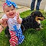 baby, child, dog, grass, outdoor, person, jeans, hand, smile, headband, blue_eyes, patriotic_clothing, stars, stripes, happy, animal, pet, street, greenery, holding_hands