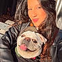 woman, dog, pug, smiling, selfie, outdoor, bench, leather_jacket, sunlight, happy, pet, tongue_out, face, long_hair, casual, daylight, portrait, cute, animal, person