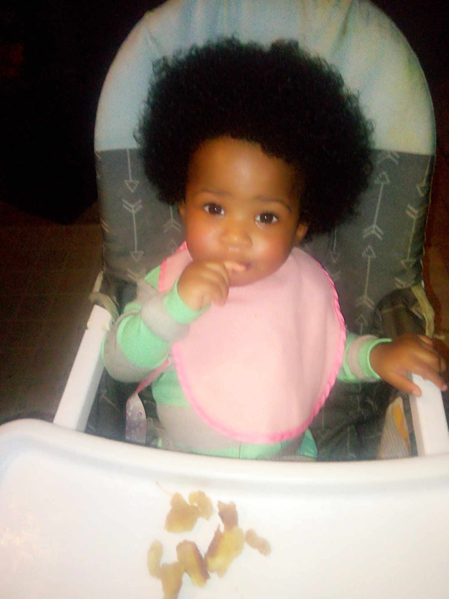 La'Nasia Major is registered to the contest to win money with this photo: baby, child, high_chair, bib, food, afro, curly_hair, indoor, feeding, tray, cute, smiling, person, infant, clothing, hand, table, face, young_child, seat