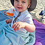 toddler, child, beach, hat, towel, blanket, sand, sun_hat, smiling, playful, outdoor, summer, sunny, young_child, clothing, person, happy, sitting, daylight, vacation