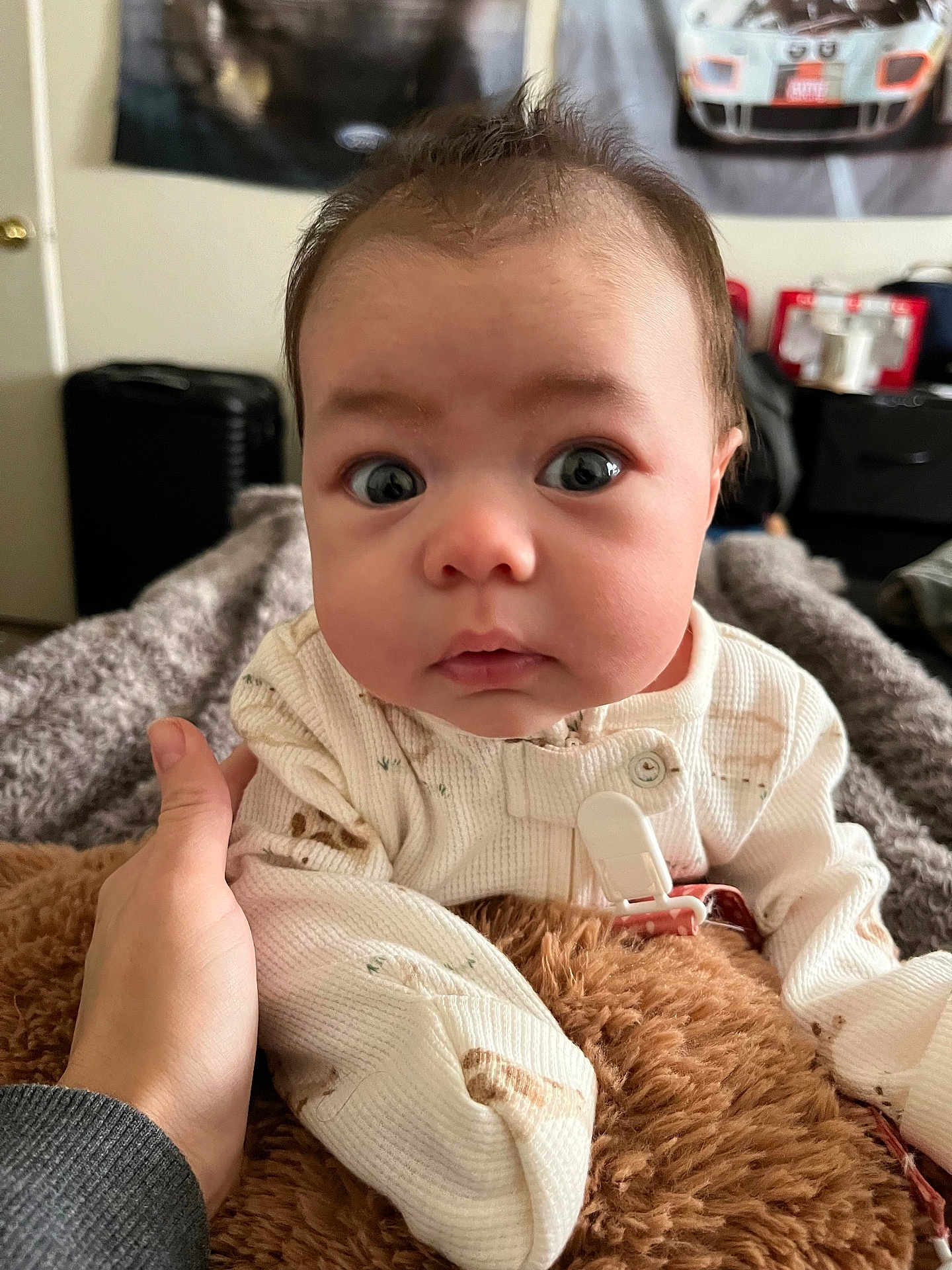 Leah is registered to the contest to win money with this photo: baby, infant, hand, blanket, white_clothing, face, wide_eyes, curious, indoor, room, poster, furniture, soft_texture, person, portrait, close_up, skin, head, expression, cozy