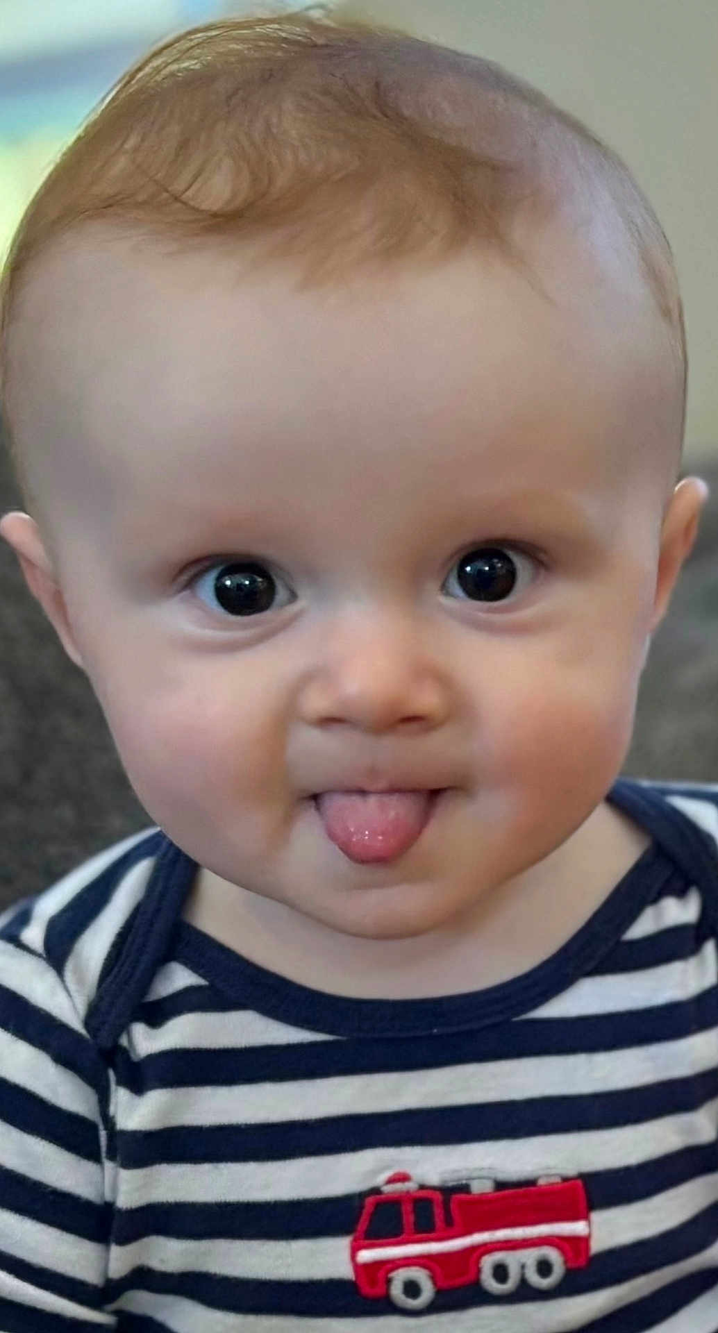 Roland is registered to the contest to win money with this photo: baby, child, tongue_out, striped_shirt, fire_truck_patch, cute, portrait, face, big_eyes, infant, cheeky, close_up, smiling, adorable, young_child, indoor, person, head, expression, clothing