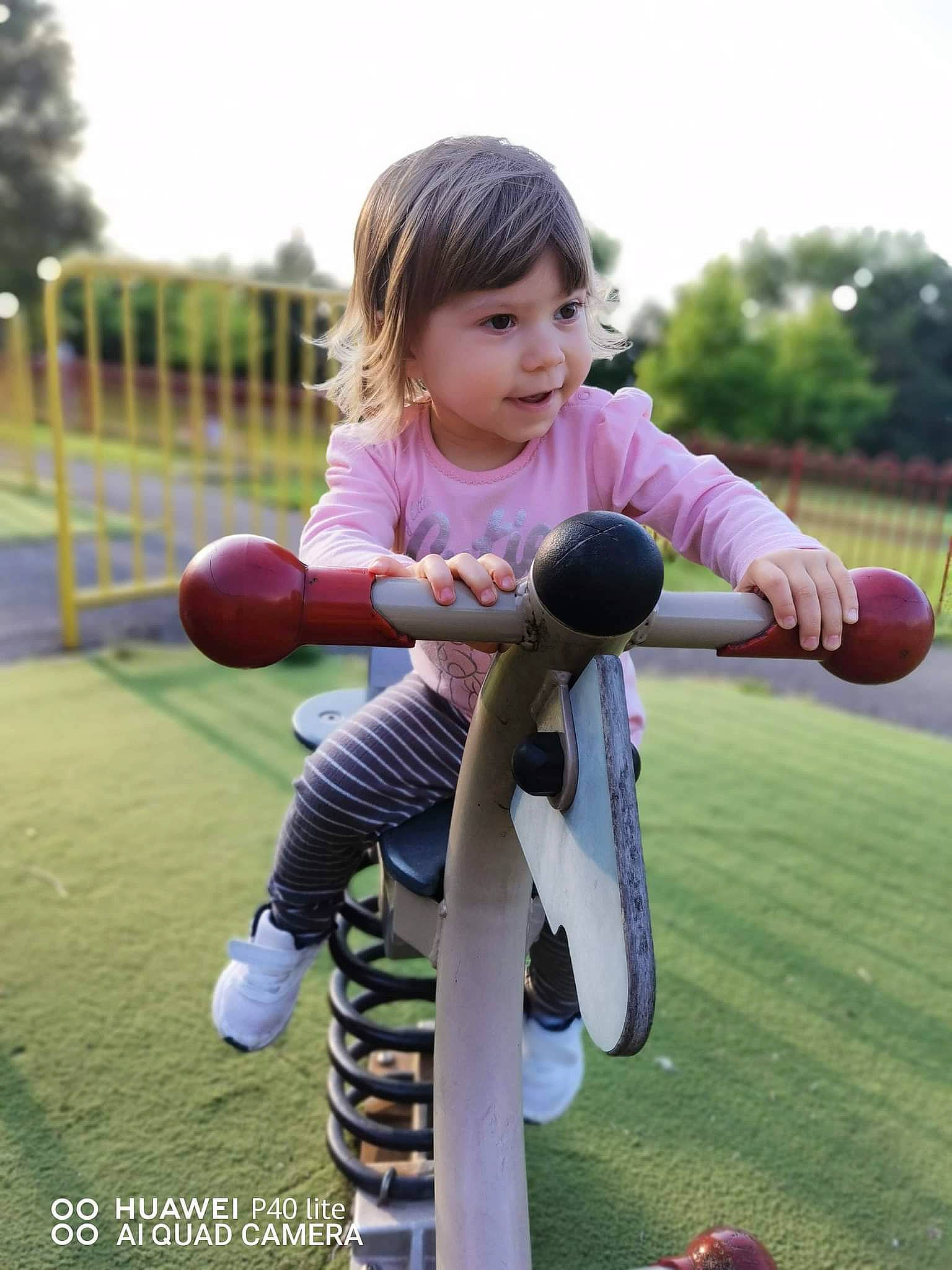 Gabriela is registered to the contest to win money with this photo: baby_toddler_clothing, child, city, face, fun, grass, happy, leisure, outdoor_play_equipment, people_in_nature, person, pink, play, recreation, sky, smile, sneakers, sock, sports_equipment, toddler